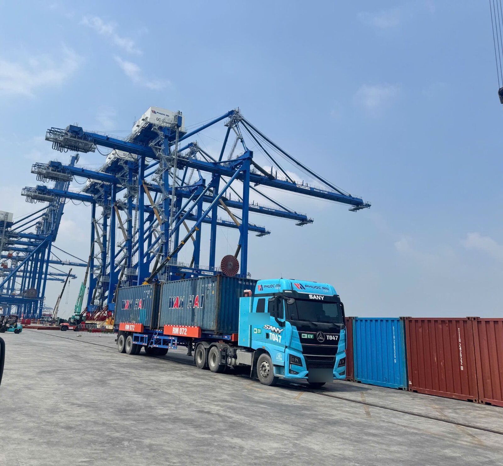Đầu kéo container gắn nhãn EV trên bãi Cảng Phước An, phía sau là dãy cẩu bờ.
