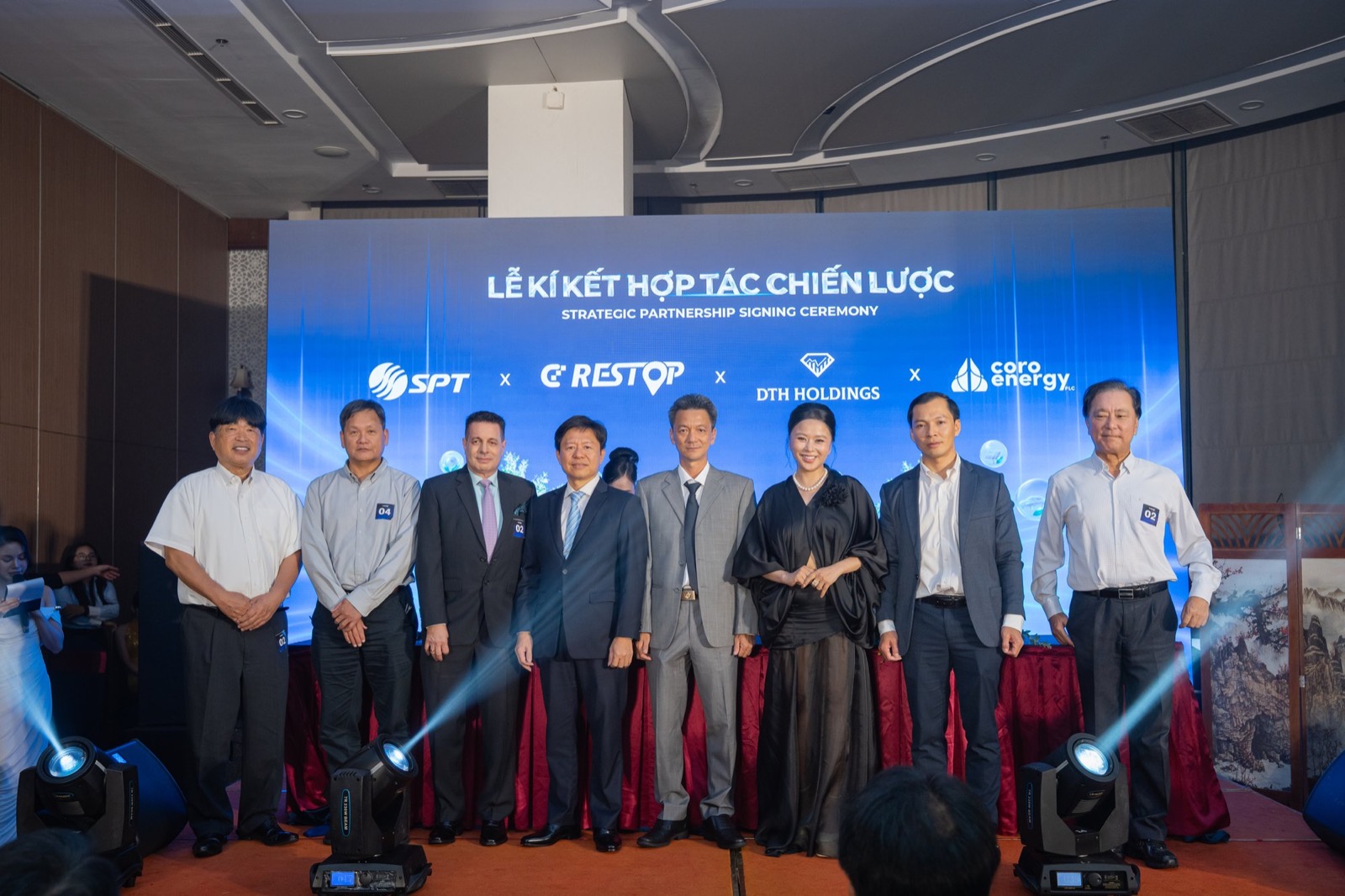 Tám đại diện các bên đứng thành hàng trên sân khấu, màn hình LED phía sau hiện logo Tập đoàn SPT, CD Restop, DTH Holdings và Coro Energy