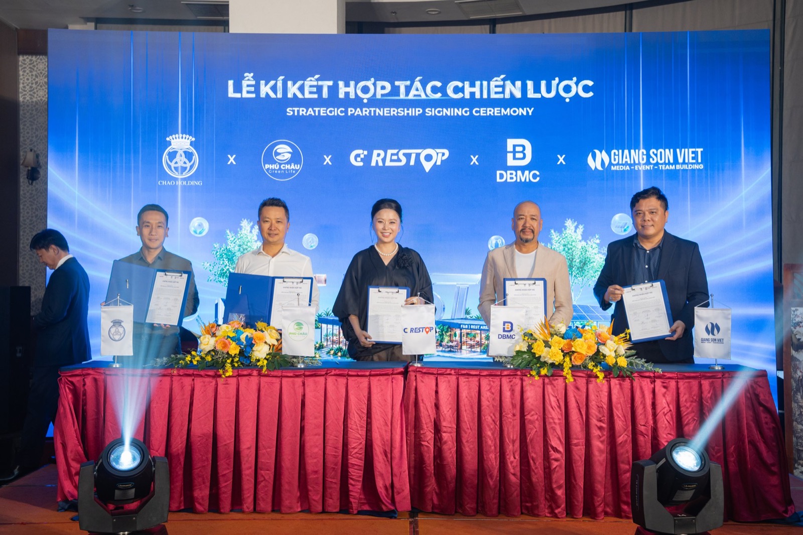 Năm đại diện đứng thành hàng giơ cao văn kiện vừa ký, cùng mỉm cười nhìn ống kính, màn hình LED phía sau hiện khối logo Chao Holding, Phú Châu, CD Restop, DBMC và Giang Sơn Việt