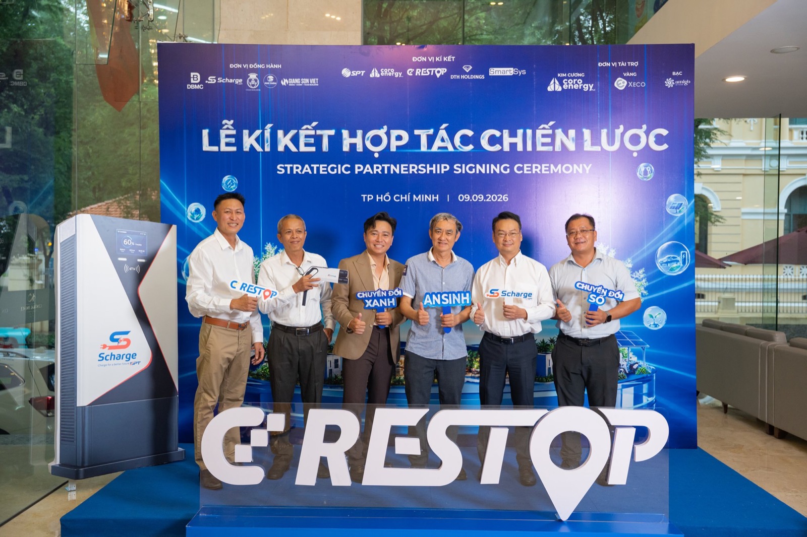 Nhóm khách mời đứng trước backdrop sự kiện, cầm các bảng chữ Chuyển đổi số, Chuyển đổi xanh, An sinh và Scharge, bên trái là trụ sạc Scharge đang trưng bày, phía trước là mô hình chữ nổi CD Restop