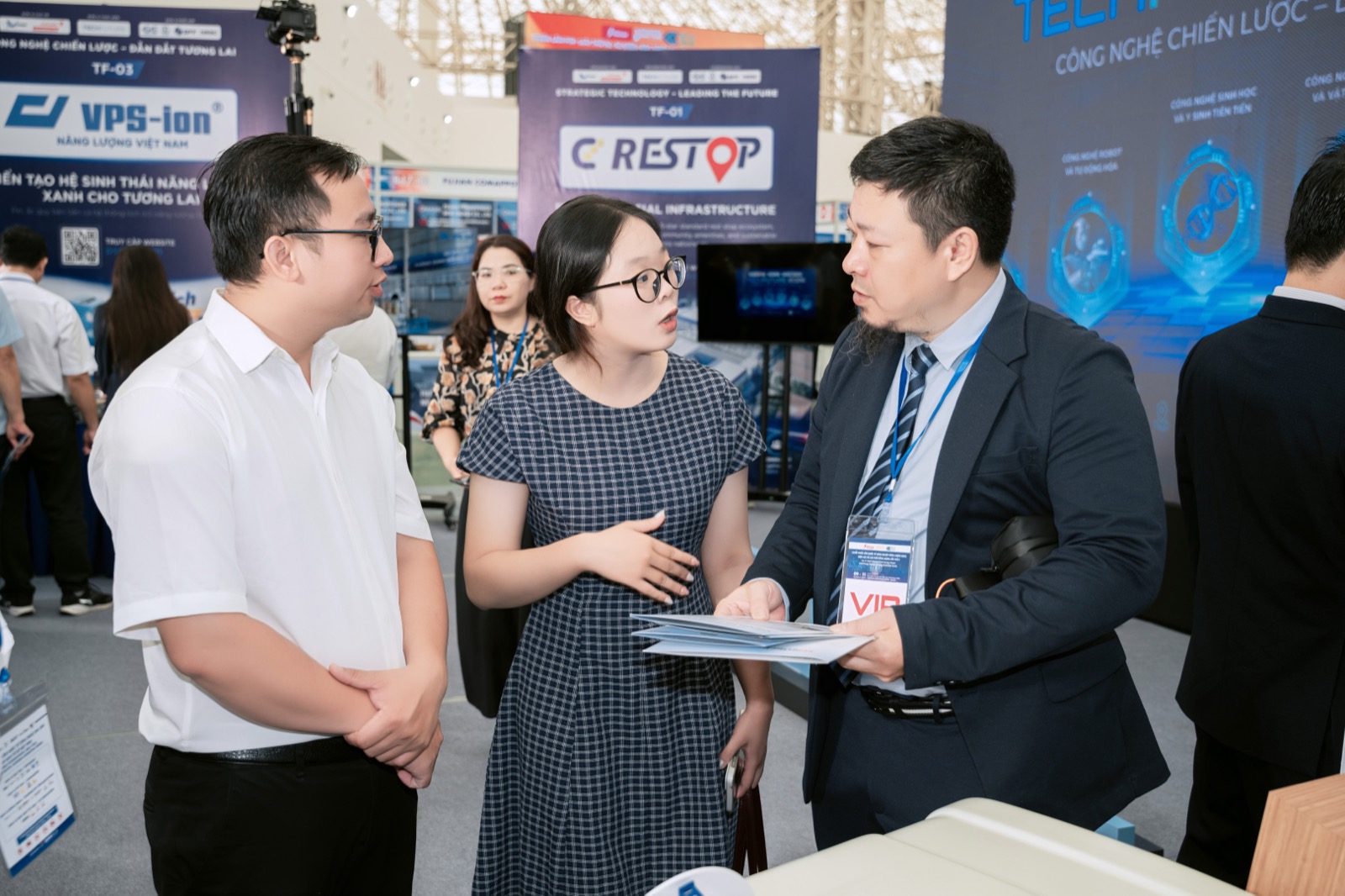Ba người trao đổi tại gian trưng bày, phía sau là standee mã TF-01 nền xanh navy mang logo CD Restop và dòng Strategic Technology – Leading the Future, bên trái là standee TF-03 của một đơn vị khác