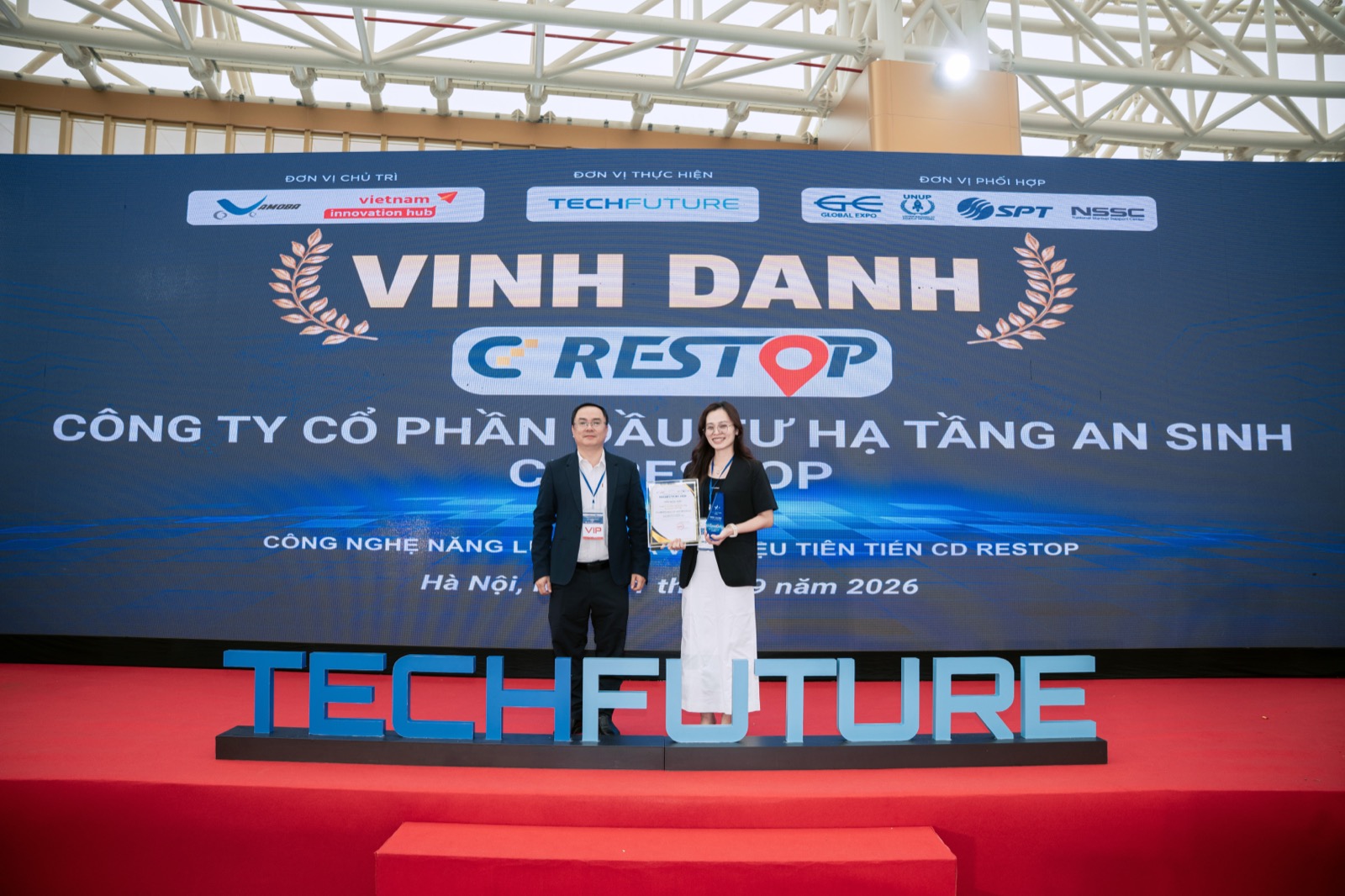 Sân khấu lễ vinh danh TechFuture 2026 với màn hình LED hiện chữ VINH DANH và logo CD Restop, hai người đứng trên sân khấu, một người cầm giấy chứng nhận và cúp